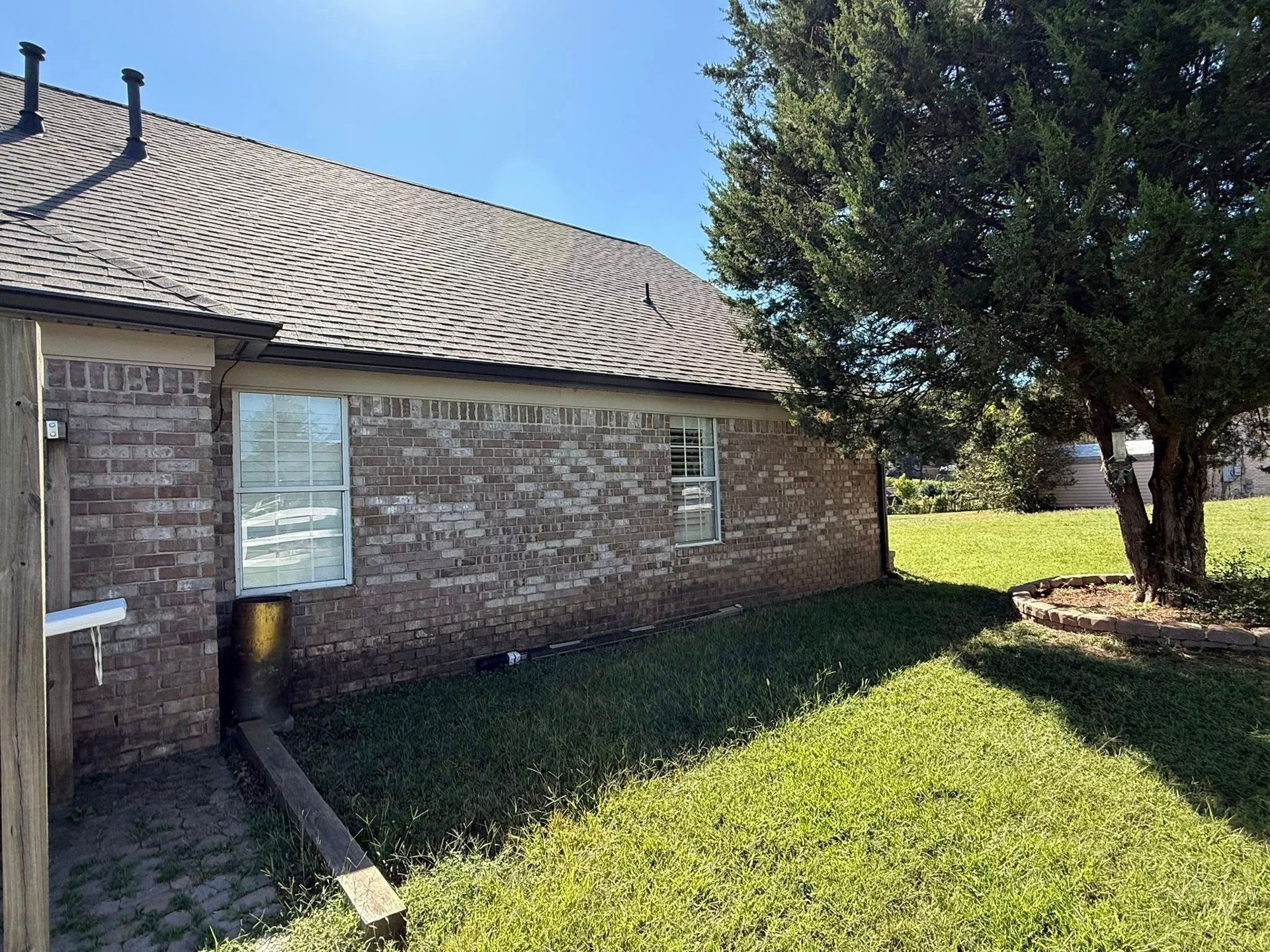 Brick building with tiled roof, grassy yard, and a large tree in bright sunlight