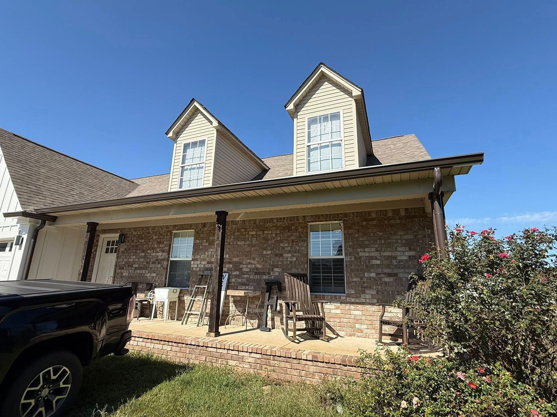 Brick house with two dormers, covered front porch, and a parked truck under a blue sky