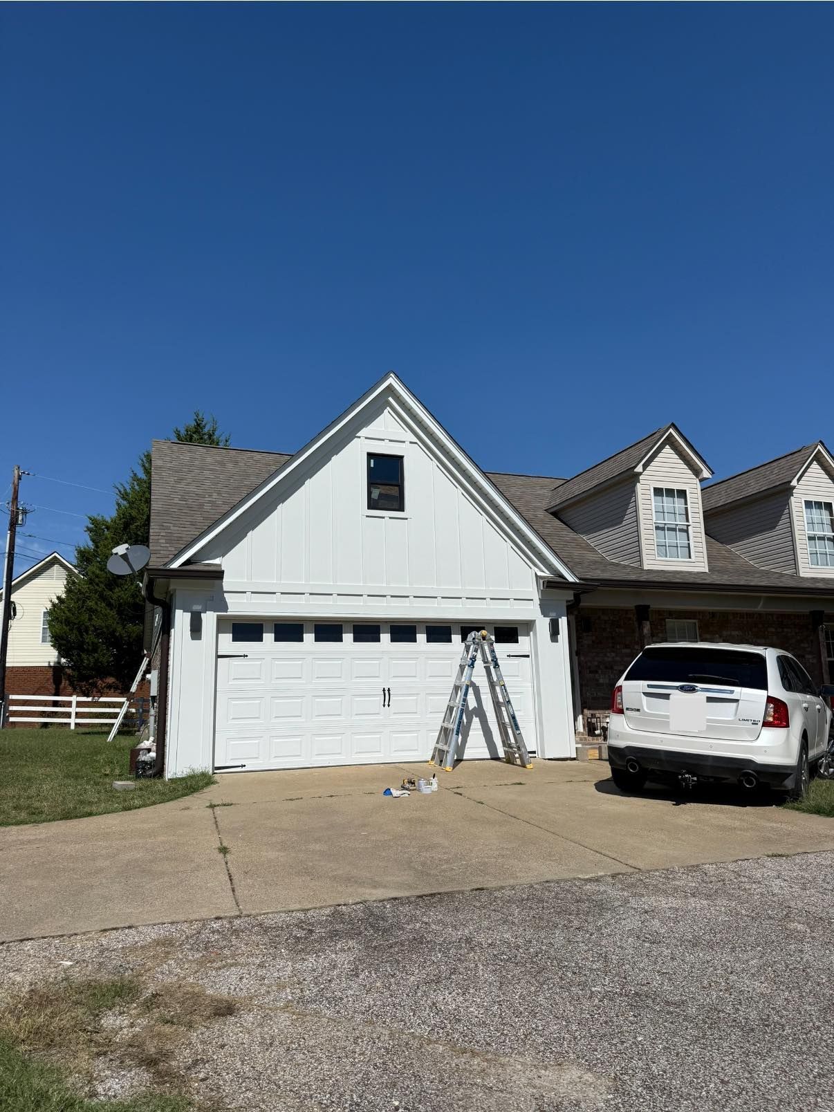 White house with attached garage and white SUV parked in driveway under a clear blue sky.