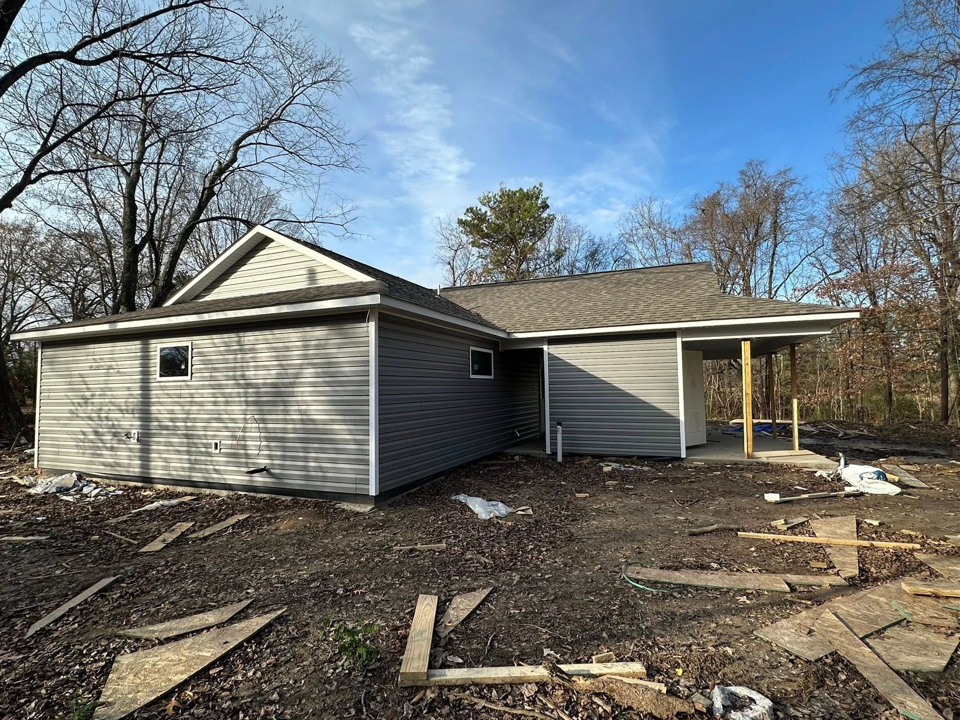 Gray house under construction with a covered porch and debris-covered yard on a clear day