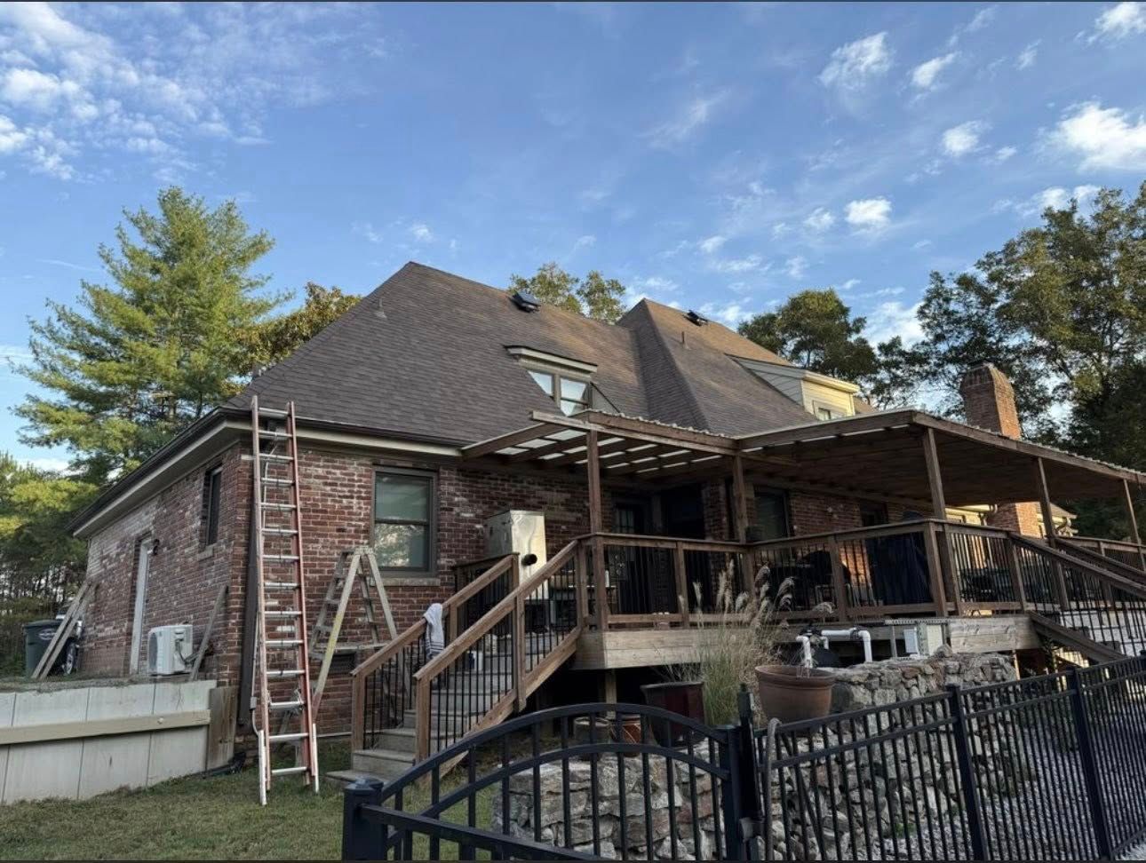 Brick house with a large deck under construction, ladders leaning against it, under a blue sky.