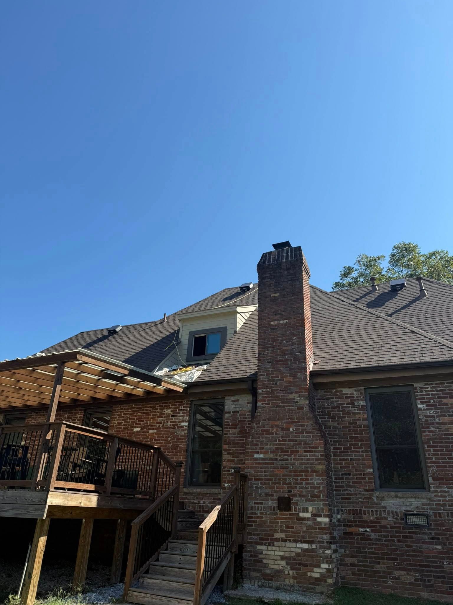 Damaged brick house with a boarded porch and broken roof under a clear blue sky