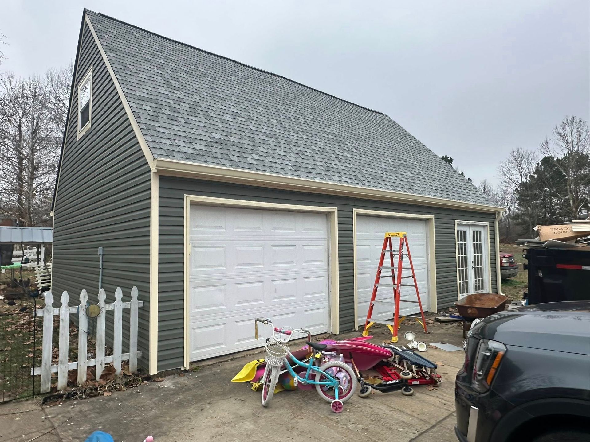 Two-car garage with a red ladder and a pile of children’s bikes and toys outside on a driveway