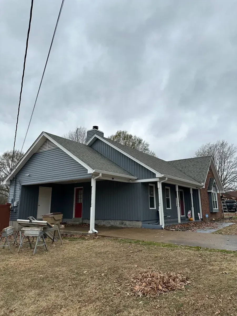 Gray house with a covered porch and white trim on a cloudy day, viewed from a front yard.