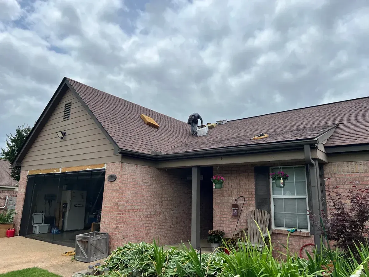 Brick house with open garage, damaged roof, and cloudy sky above
