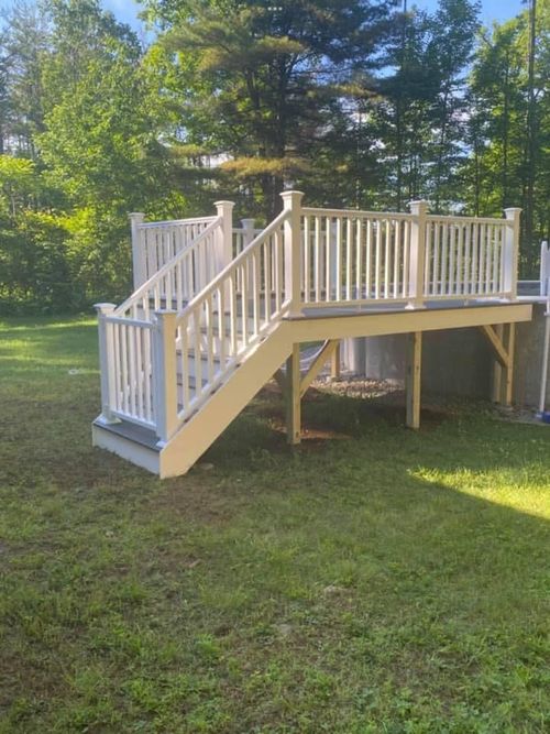 A white wooden deck with a staircase and gate leading to an above-ground pool in a grassy backyard.