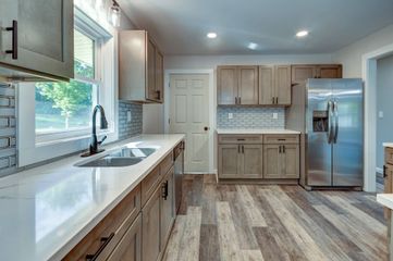 A modern kitchen with light wood cabinets, white countertops, stainless steel refrigerator, and wood-look plank flooring.