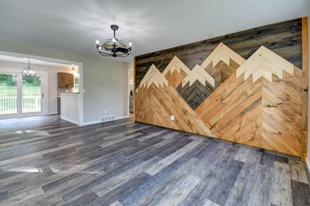 A room with gray wood-look flooring and a feature wall showcasing a large, wood-plank mountain range art installation.