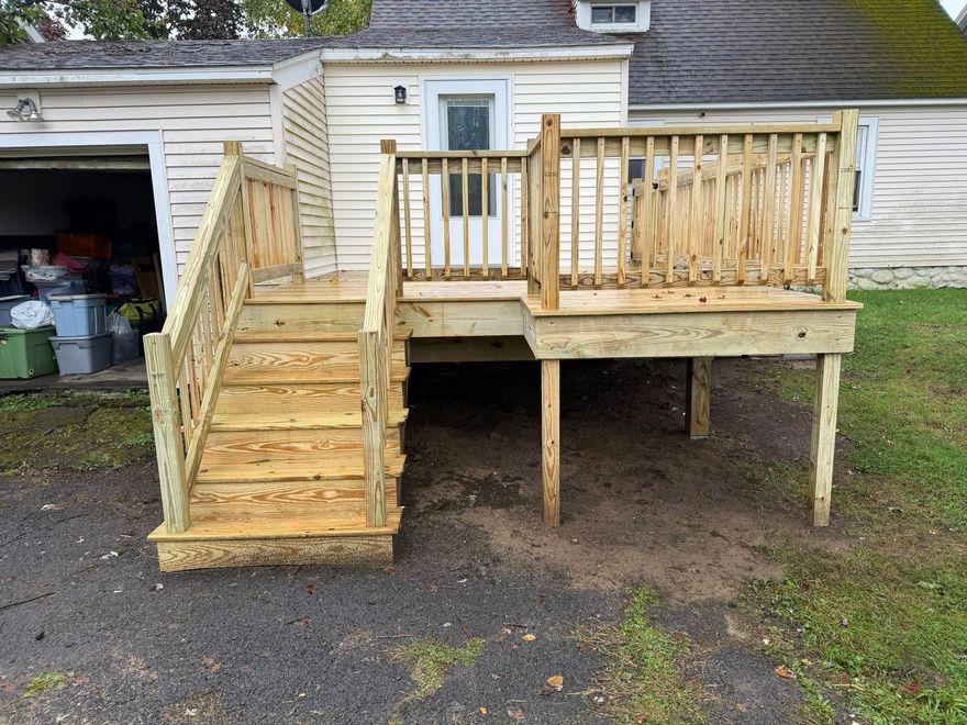 Newly constructed wooden deck with stairs and railing attached to the back of a house.