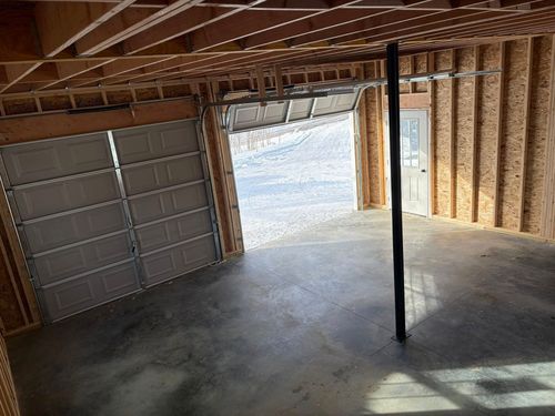 An unfinished garage with exposed wood framing, a closed sectional garage door, a partial open door, and a support post.