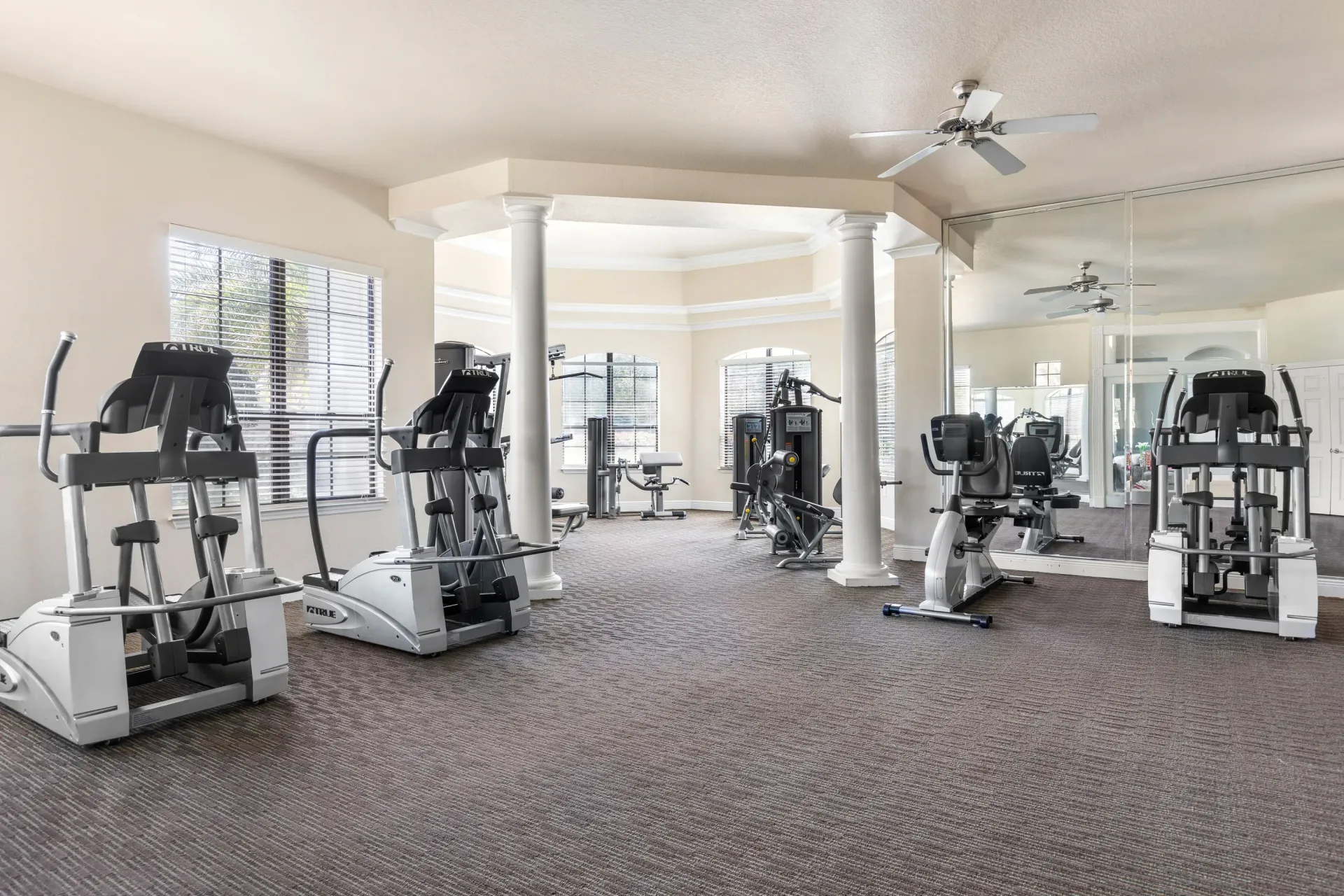 Bright home gym with several treadmills and exercise machines on carpeted floor at Levi at River City.