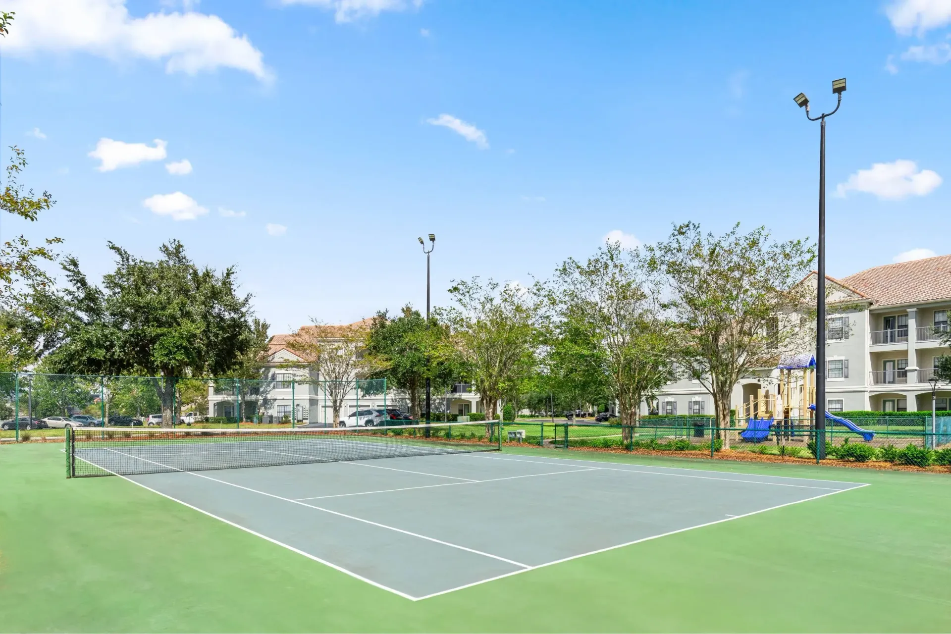 Tennis court with a playground in the background at Levi at River City.