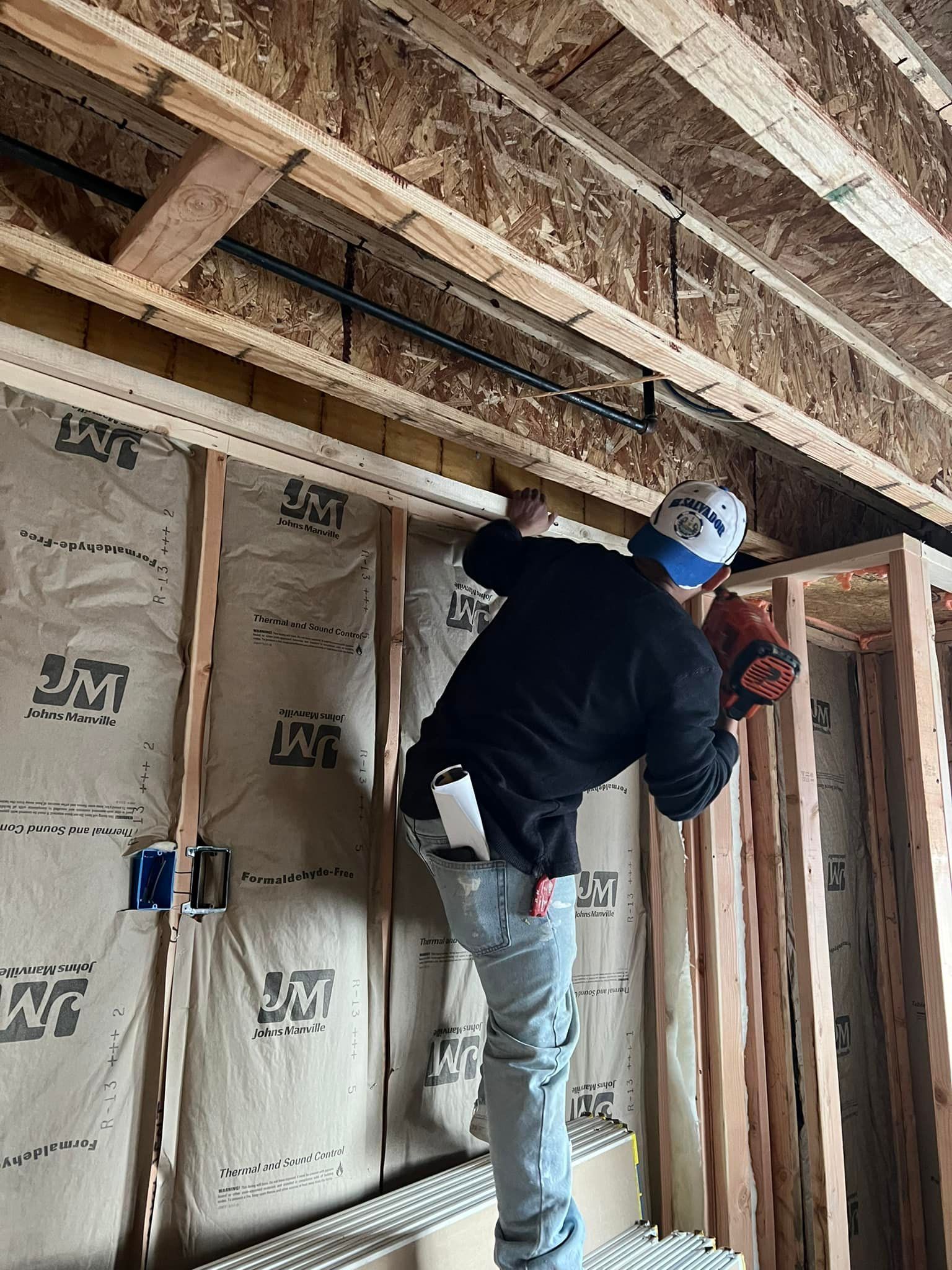 A man is standing on a ladder in a room under construction.