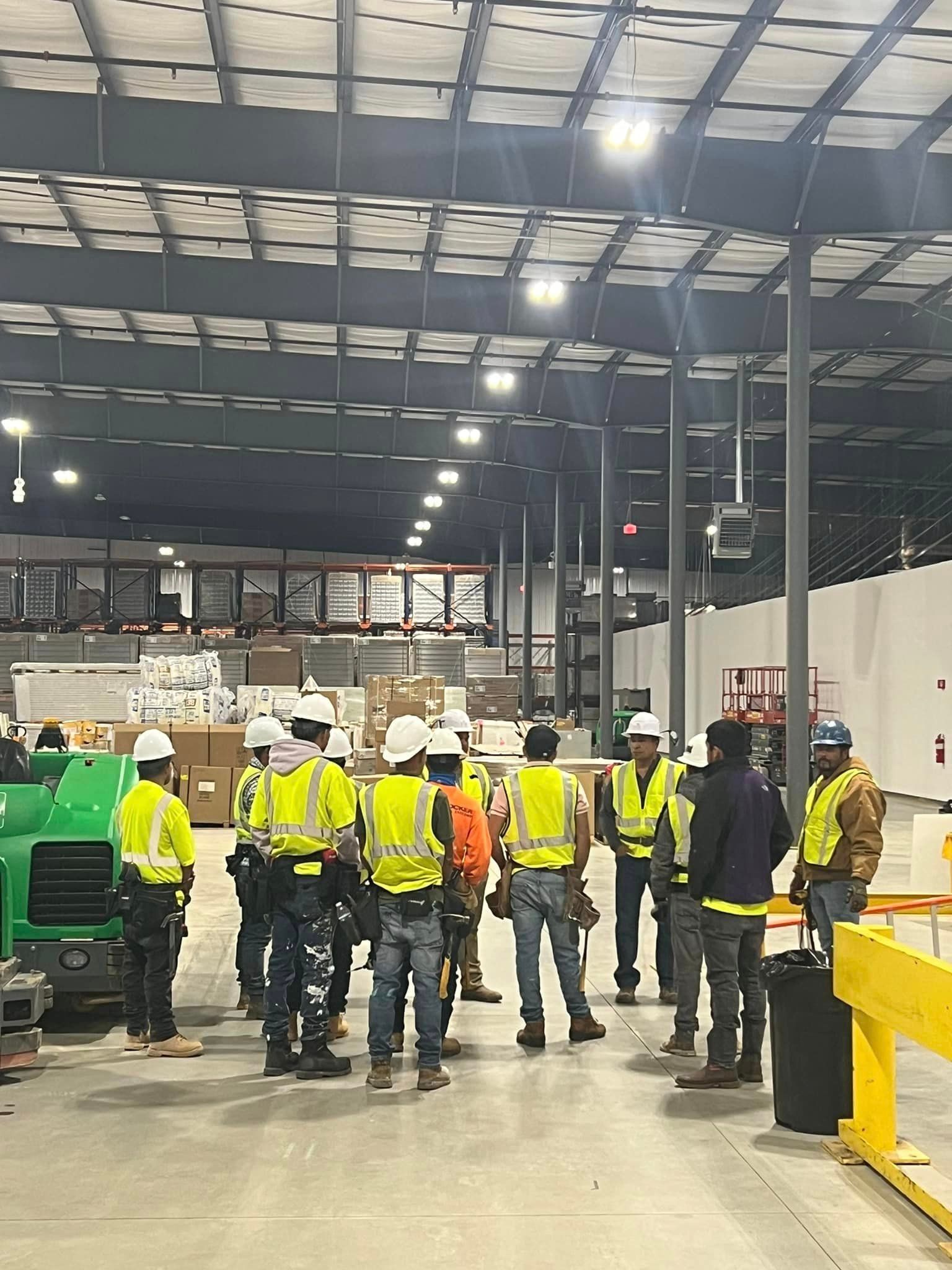 A group of construction workers are standing in a large warehouse.