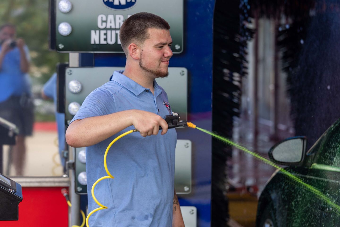 A man is washing a car with a hose at a car wash.