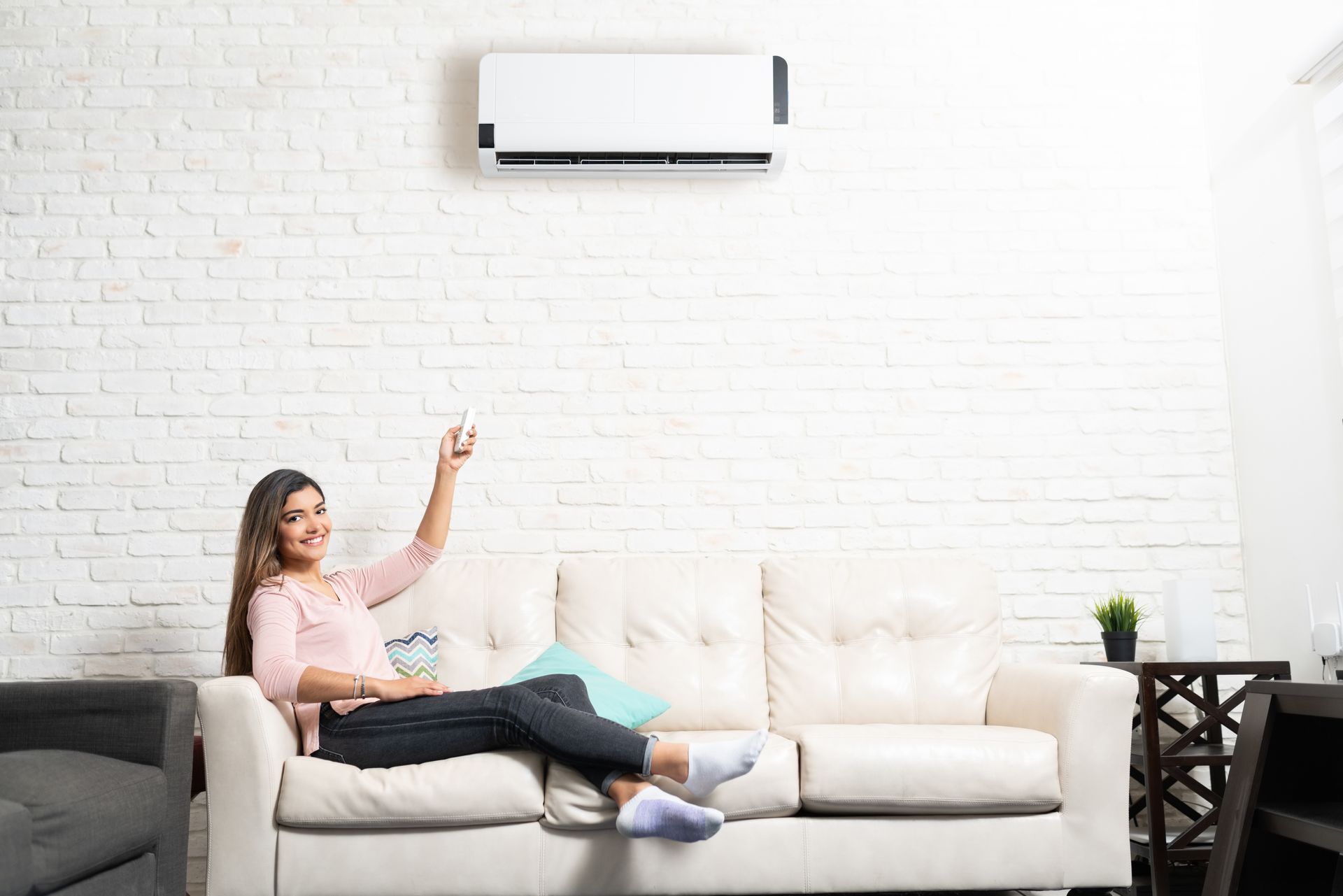 woman using mini-split ac from couch with a remote