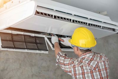 A worker using tool on an AC unit