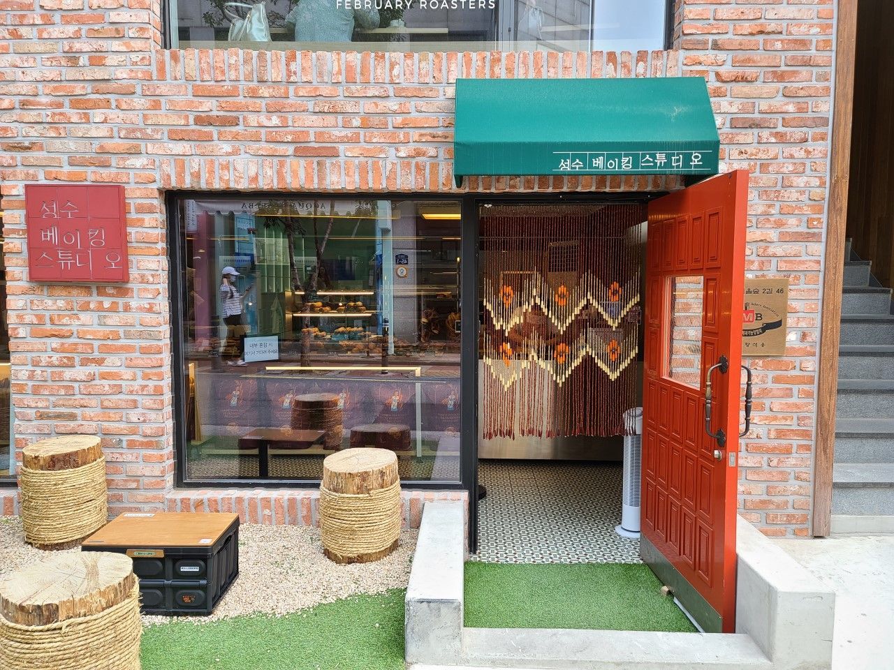 Exterior of Seongsu Baking Studio with red brick walls, green awning, and rustic outdoor seating nea