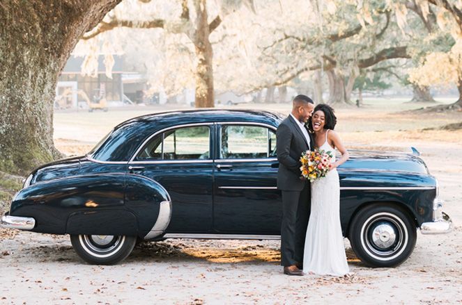 A bride and groom are posing for a picture in front of an old car.