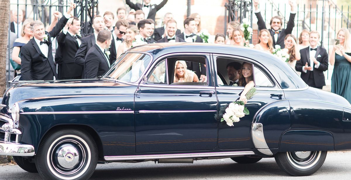 A bride and groom are getting out of an old black car.