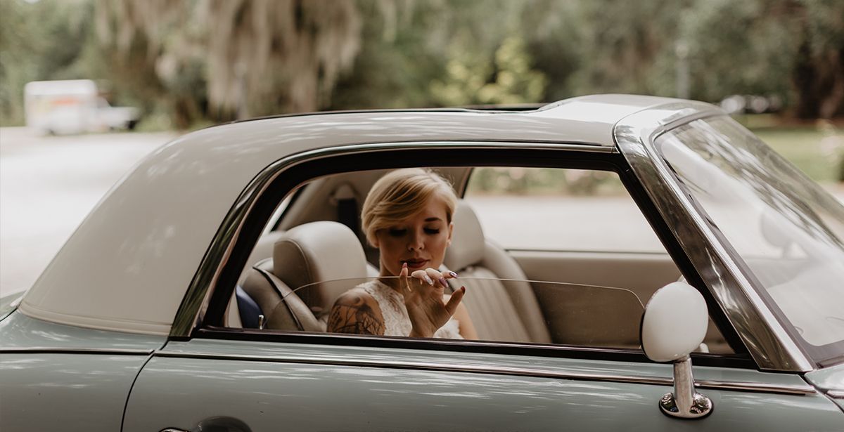 A woman is sitting in the back seat of a car applying lipstick.