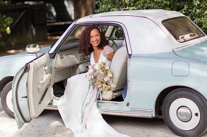 A bride in a wedding dress is getting out of a blue car.