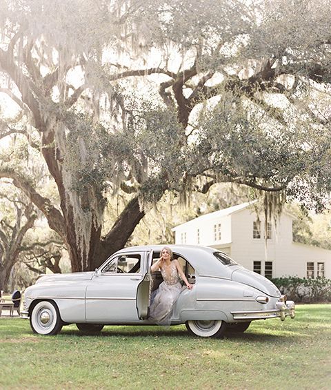 A bride and groom are getting out of an old white car.