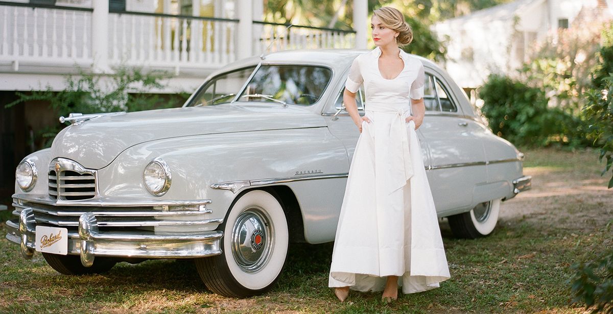 A woman in a white dress is standing next to a white car.