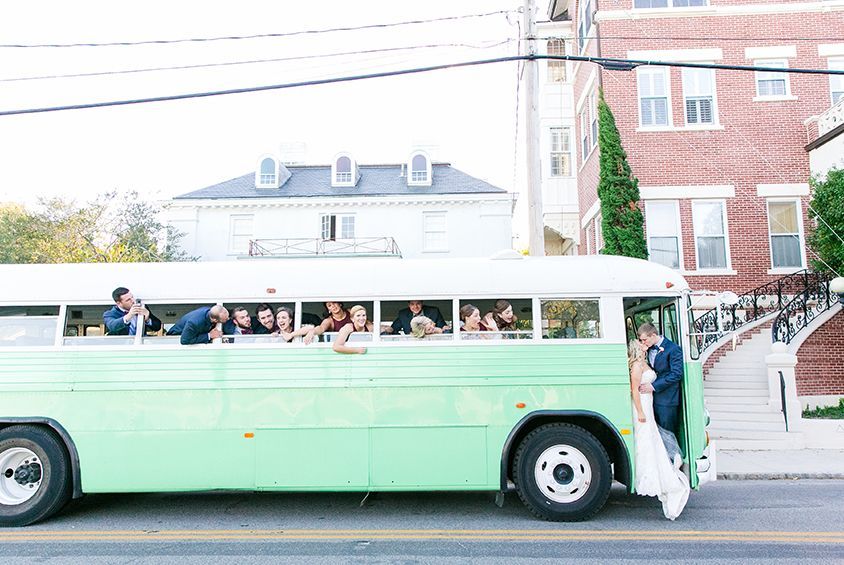 A bride and groom are kissing in front of a green bus.