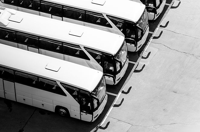 A black and white photo of a row of buses parked in a parking lot.