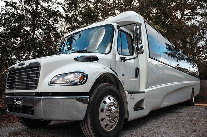 A white bus is parked on a gravel road in front of trees.