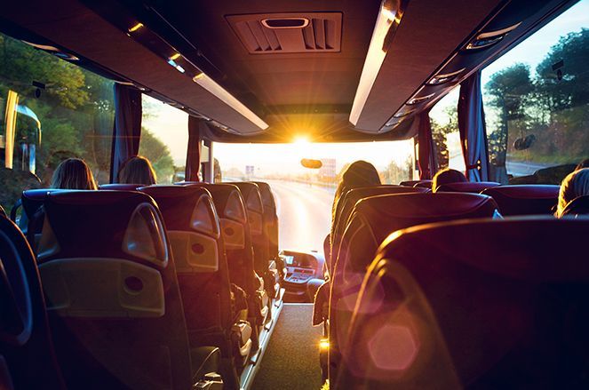 The sun is shining through the windows of a bus filled with people.