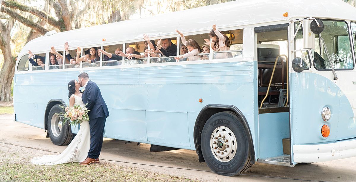 A bride and groom are kissing in front of a blue bus.