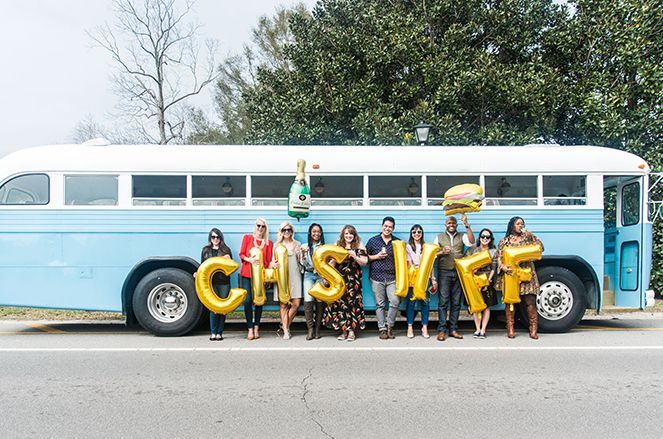 A group of people are standing in front of a blue bus holding balloons that spell out the word cashmere.