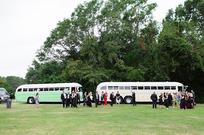 A group of people are standing in front of two buses in a field.