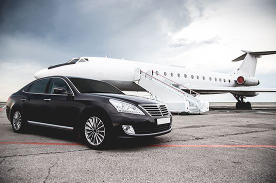 A black car is parked in front of a private jet.