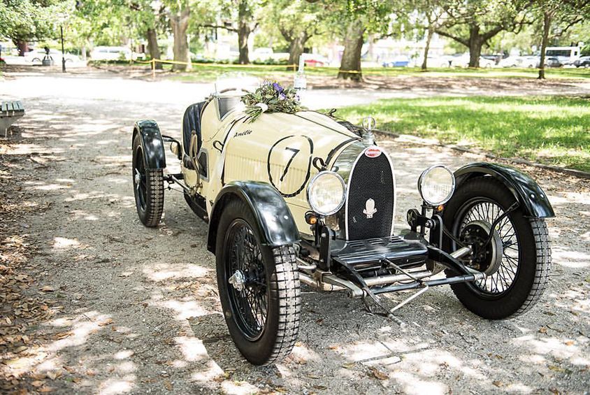 An old race car is parked on a dirt road in a park.