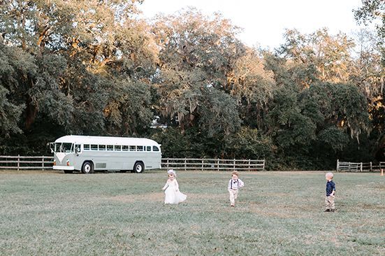 A group of children are running in a field in front of a white bus.