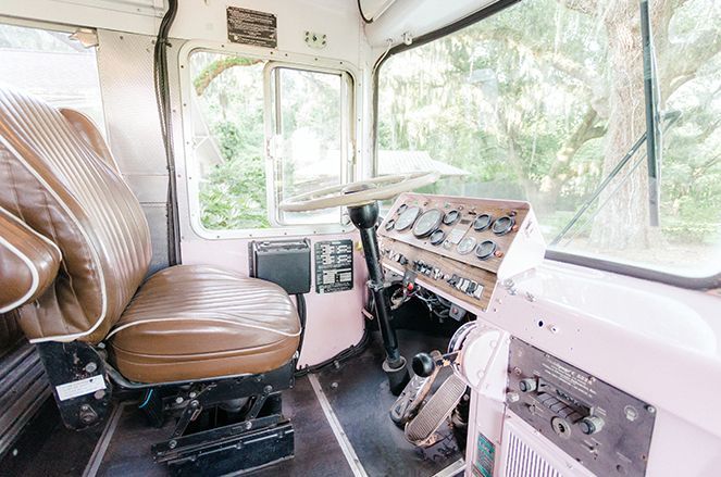 The inside of a pink bus with a brown seat and a steering wheel.