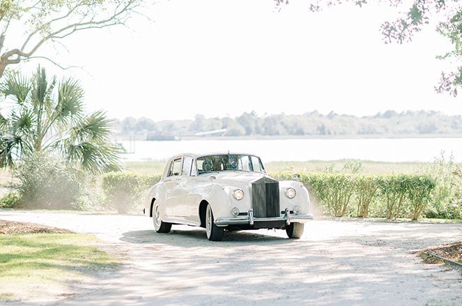 A white rolls royce is driving down a dirt road.
