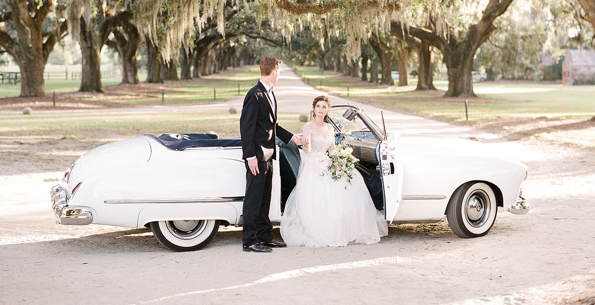 A bride and groom are standing next to a white car.