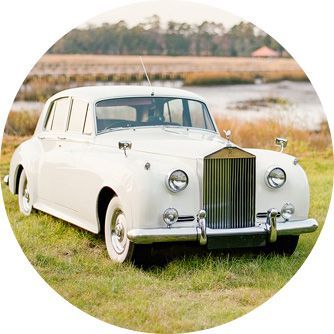 A white rolls royce is parked in a grassy field.