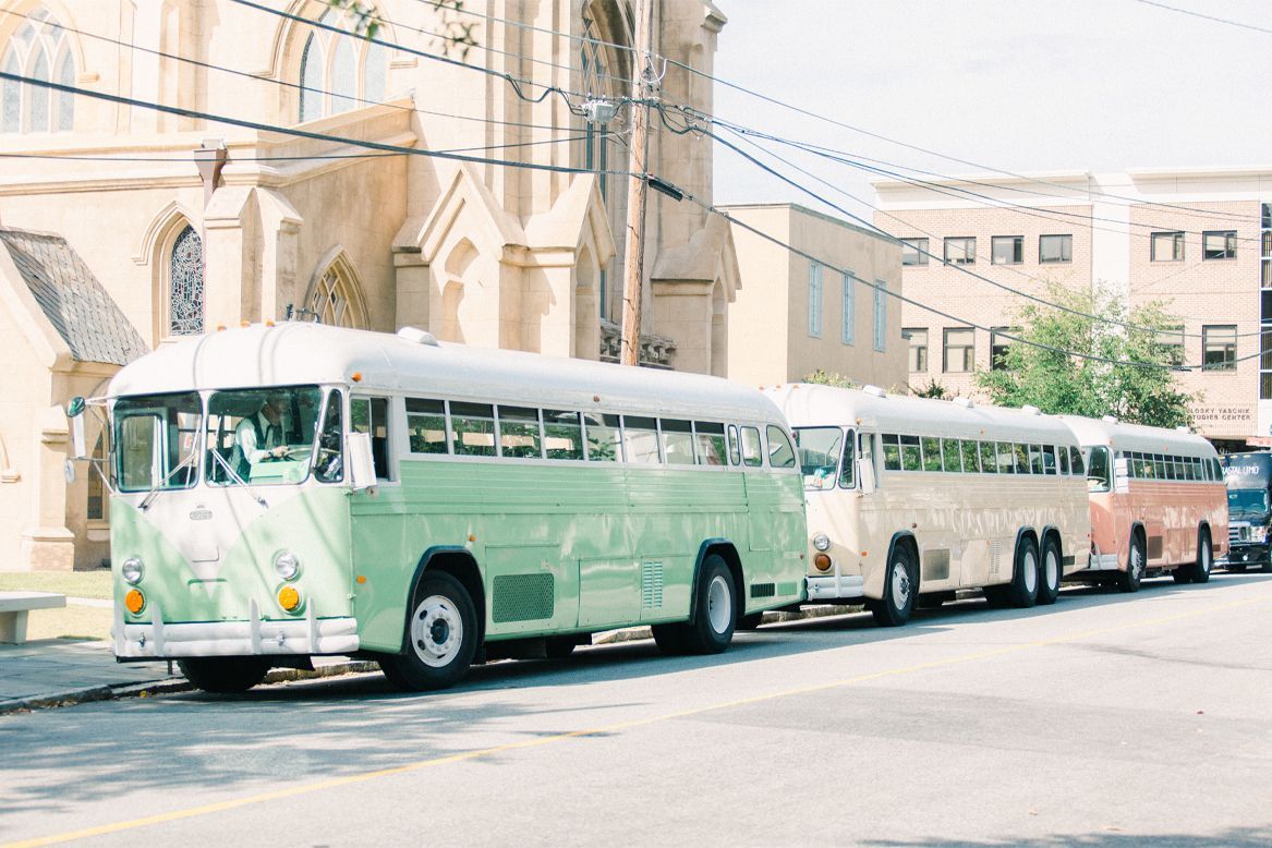 Three buses are parked on the side of the road in front of a church.