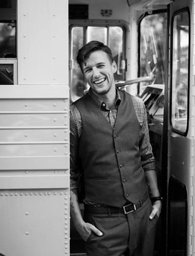 A man in a vest is standing in the doorway of a bus.