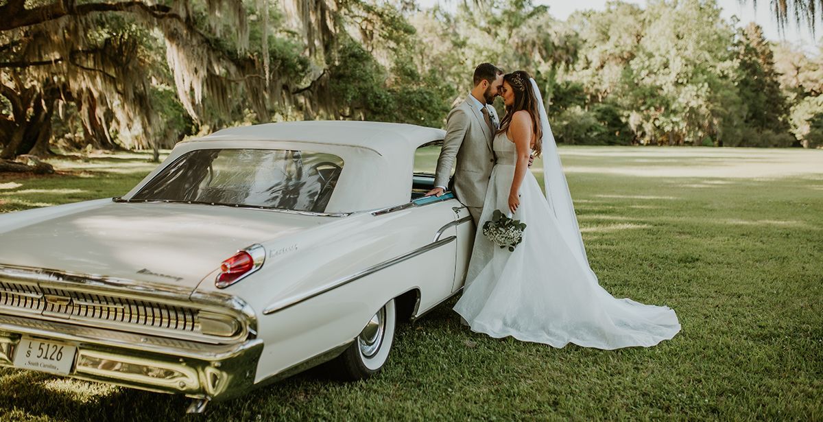 A bride and groom are kissing in front of a white car.