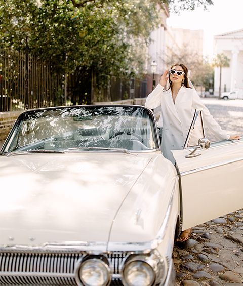 A woman is standing next to a white convertible car.