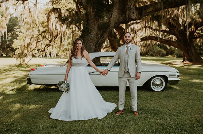 A bride and groom are holding hands in front of a white car.