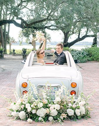 A bride and groom are sitting in a white car decorated with flowers.