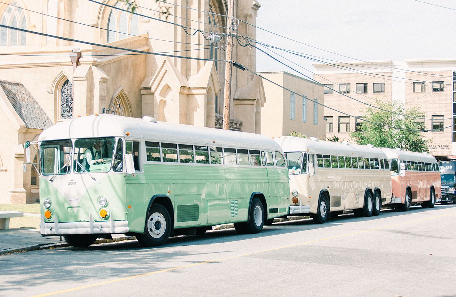 A row of buses are parked on the side of the road in front of a church.