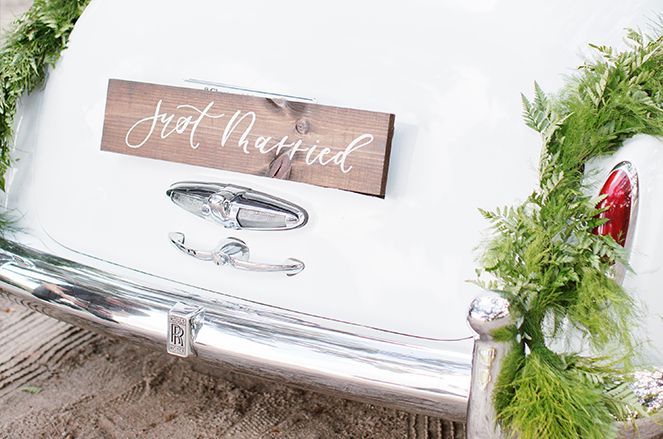 A white car with a wooden sign on the back that says `` just married ''.